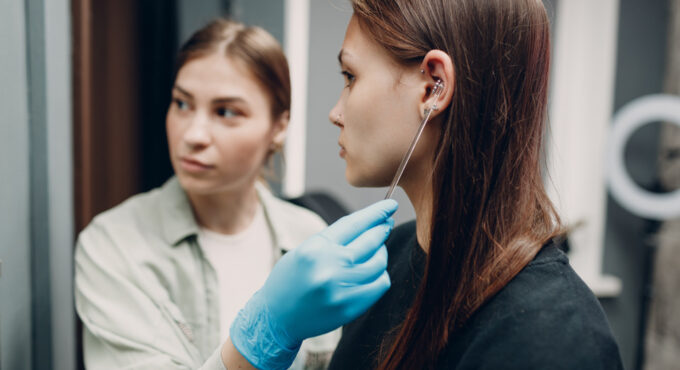 Młoda kobieta przymierza się do wykonania przekłucia uszu w salonie piercingu